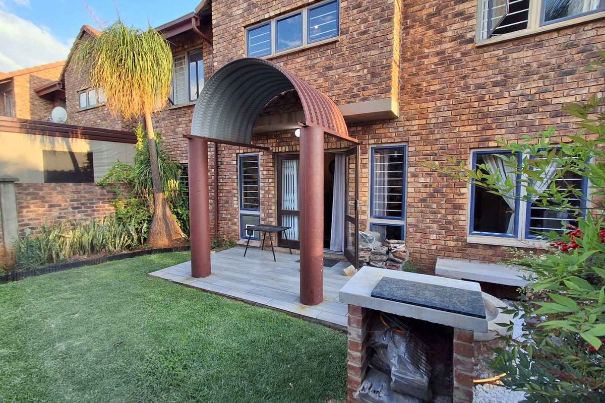 Rear exterior view of a face brick townhouse featuring a tiled patio with a unique arched metal cover and a built-in brick braai area.