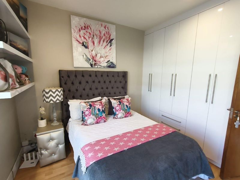 A well-maintained bedroom featuring light hardwood flooring, ample built-in white cabinetry, and floating shelving for storage.