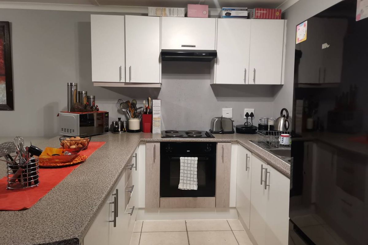 Compact kitchen featuring white cabinetry, a built-in oven, electric hob, extractor fan, and durable stone-look countertops with tiled flooring.