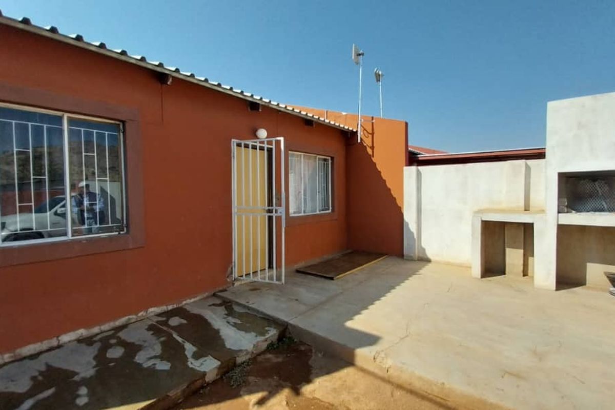 Rear exterior view of the apartment featuring a concrete patio area with a built-in braai and security gates on windows and doors.