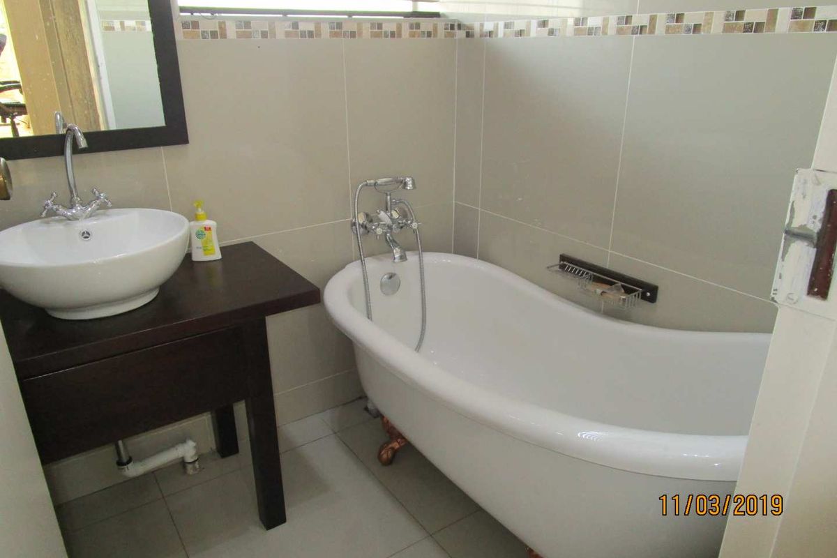 A bathroom featuring a freestanding bathtub, a vessel sink on a dark wood vanity, and neutral wall tiling.