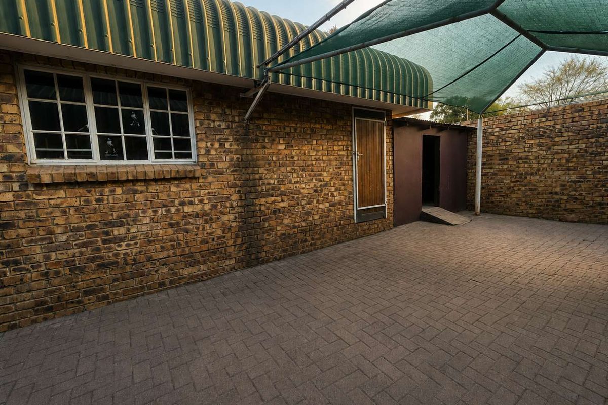 A paved rear courtyard featuring face brick walls, a corrugated metal roof section, and a shade cloth canopy structure.