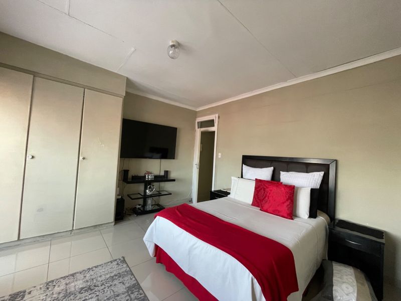 A bedroom featuring tiled flooring, built-in cupboards, and a coved ceiling, offering a functional space with potential for cosmetic updates.