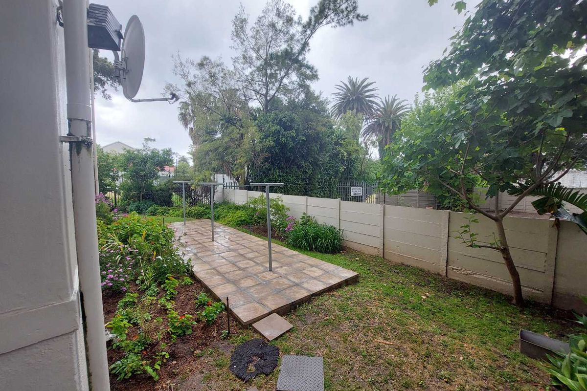 A rear garden area featuring a paved patio section, metal washing lines, and a precast concrete boundary wall with established garden beds.