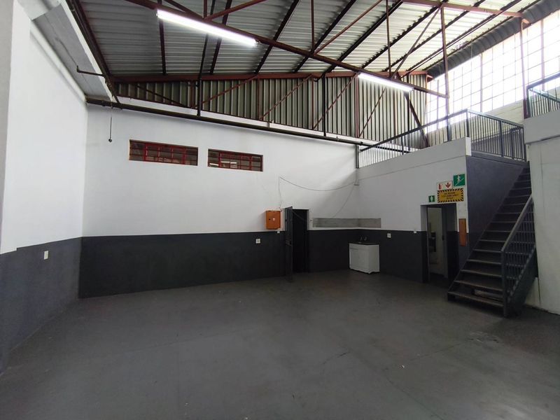 Spacious industrial utility area featuring high ceilings with exposed steel trusses, a mezzanine level accessed by a steel staircase, and durable epoxy flooring.