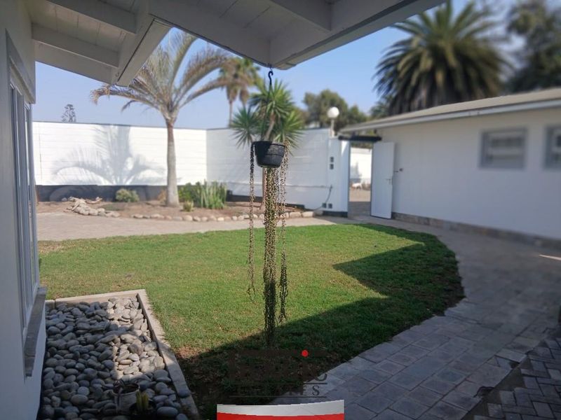 A view of the rear garden featuring a paved walkway, lawn area, and a covered patio space.