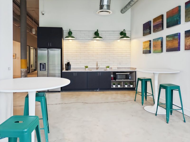 Modern office kitchenette featuring dark cabinetry, subway tile backsplash, polished concrete floors, and industrial-style exposed ductwork with contemporary lighting.