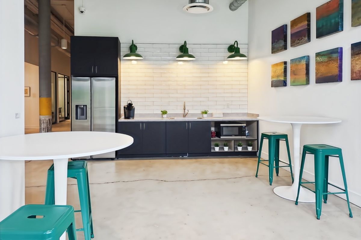 Modern office kitchenette featuring dark cabinetry, subway tile backsplash, polished concrete floors, and industrial-style exposed ductwork with contemporary lighting.