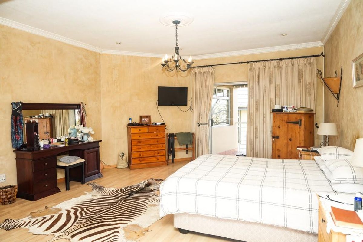 Spacious bedroom featuring laminate flooring, decorative ceiling rose with chandelier, and direct access to an outdoor balcony through sliding glass doors.