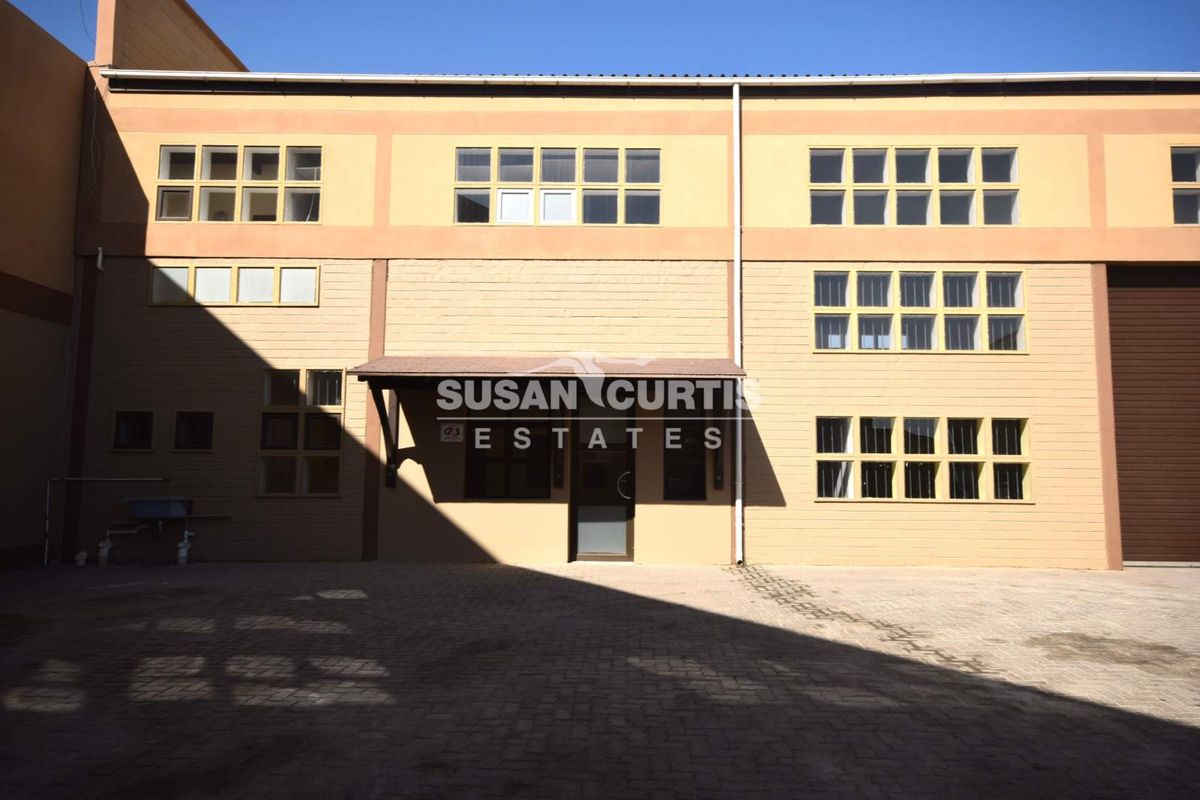 Front elevation of a multi-story industrial building featuring a paved entrance area, large multi-pane windows, and a covered entryway.