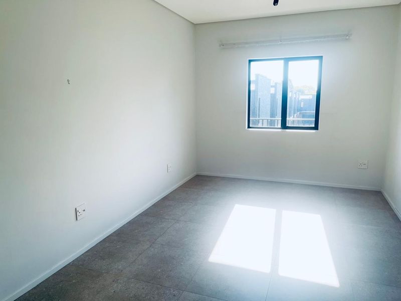 A bright, empty bedroom featuring neutral tiled flooring, clean white walls, and a modern aluminium-framed window.
