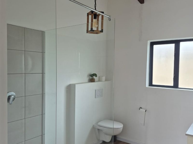 Modern bathroom featuring a glass-enclosed shower with pebble flooring, wall-mounted toilet, and exposed timber ceiling beams, creating a bright and contemporary aesthetic.