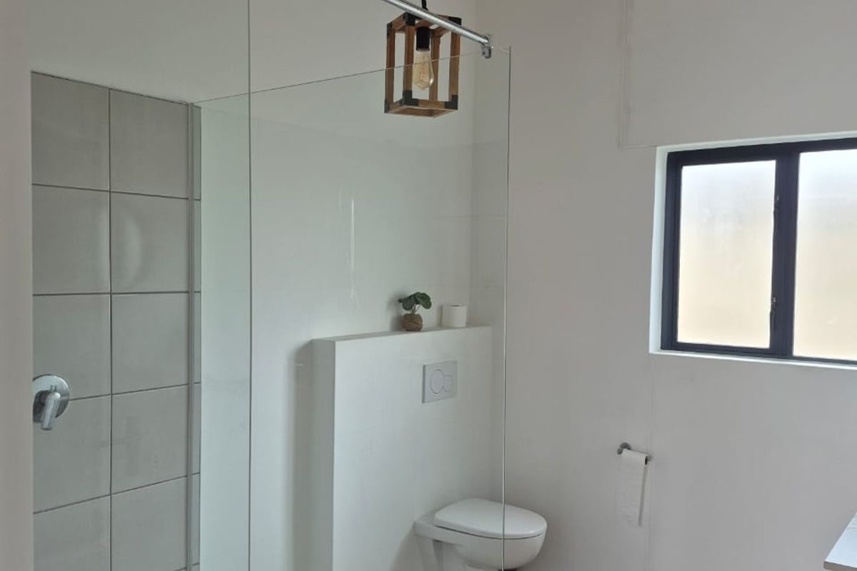 Modern bathroom featuring a glass-enclosed shower with pebble flooring, wall-mounted toilet, and exposed timber ceiling beams, creating a bright and contemporary aesthetic.
