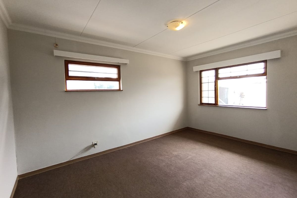 A clean, empty bedroom featuring neutral walls, carpeted flooring, and timber-framed windows, offering a blank canvas for personalization.
