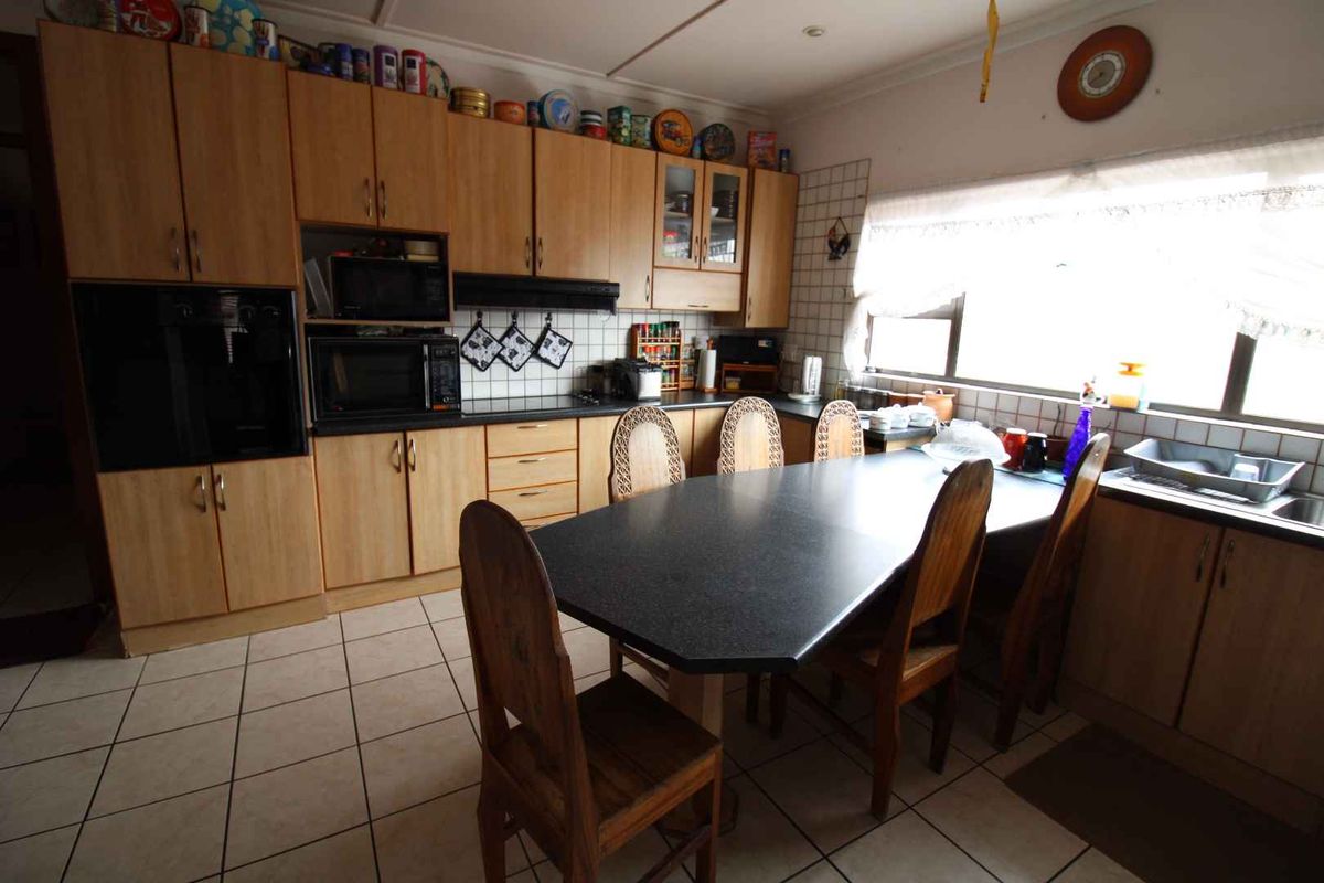 A functional kitchen featuring wood-look cabinetry, integrated oven, dark laminate countertops, and tiled flooring with an attached dining area.