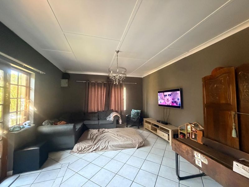 A living room featuring tiled flooring, a central light fixture, and a wall-mounted television, offering a functional space with potential for cosmetic updates.