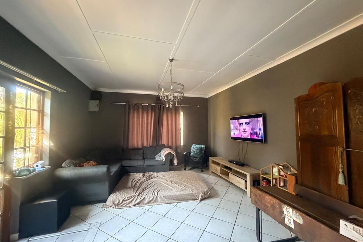 A living room featuring tiled flooring, a central light fixture, and a wall-mounted television, offering a functional space with potential for cosmetic updates.