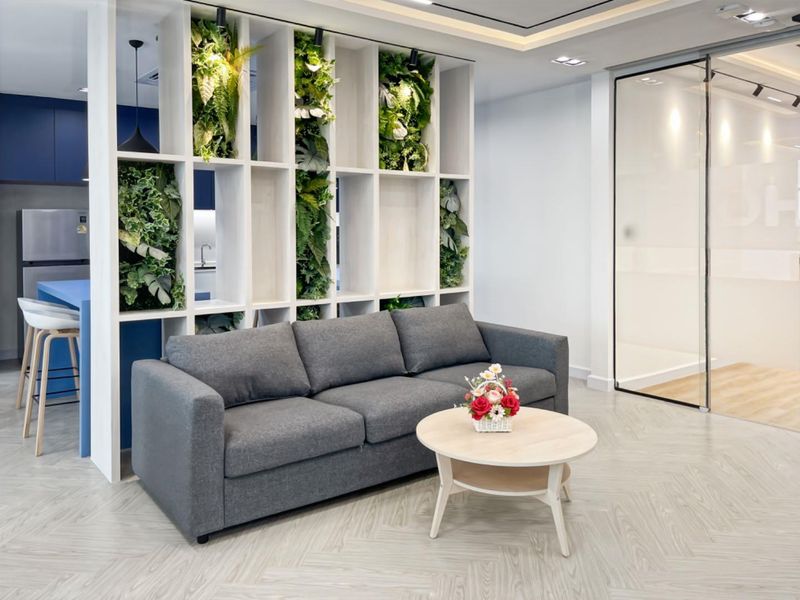 Modern open-plan office space featuring a decorative built-in shelving unit with integrated greenery, herringbone flooring, and a sleek glass partition wall.