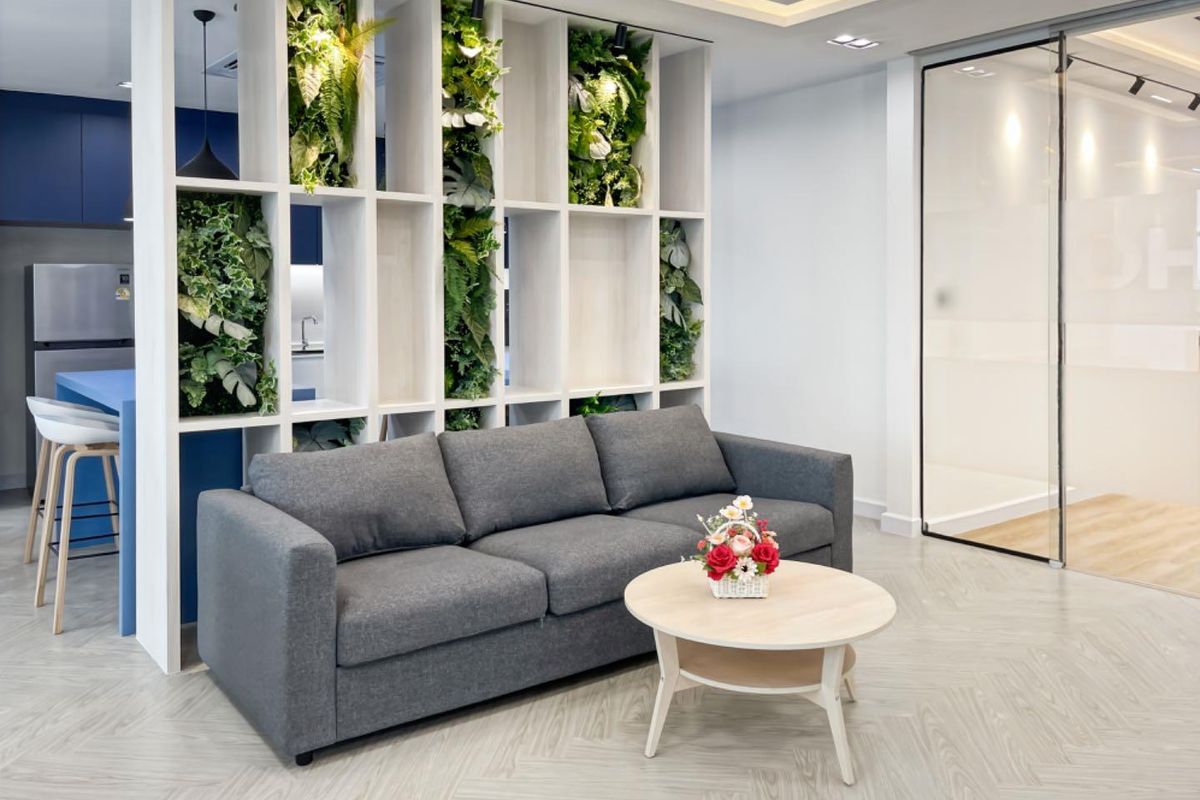 Modern open-plan office space featuring a decorative built-in shelving unit with integrated greenery, herringbone flooring, and a sleek glass partition wall.