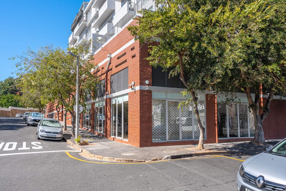 Street-level view of a modern retail property featuring a red brick facade, large glass storefront windows, and integrated security shutters.