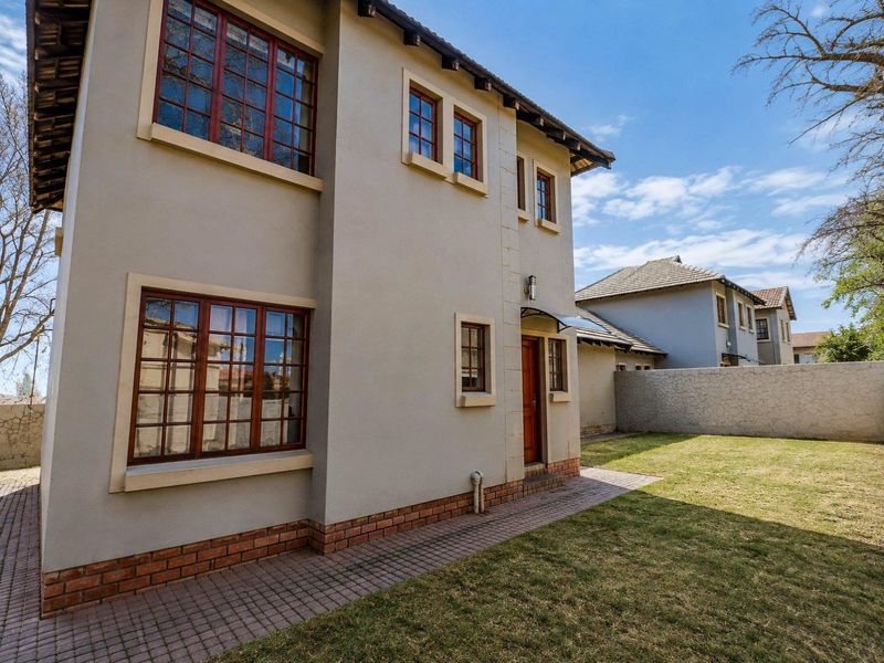 Rear view of a double-story house featuring a paved walkway, well-maintained lawn, and secure boundary wall.