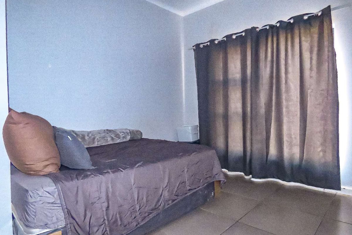 A bedroom featuring tiled flooring and large sliding glass doors covered by curtains, providing access to an outdoor area.