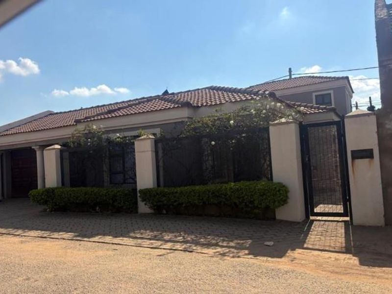 Front elevation of a residential house featuring a tiled roof, paved driveway, boundary wall with pedestrian gate, and integrated garage.