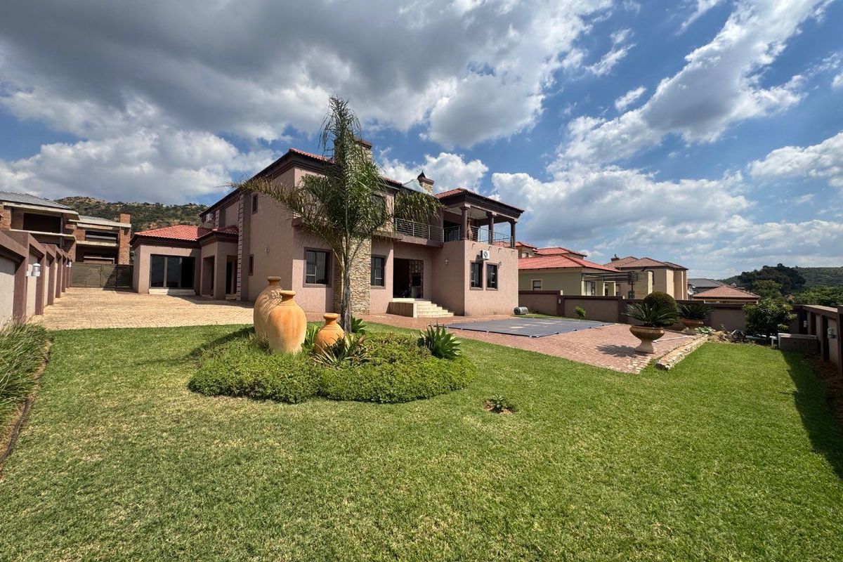 Spacious rear exterior view featuring a landscaped garden, paved patio area, swimming pool, and a multi-level residence with balcony and stone facade details.
