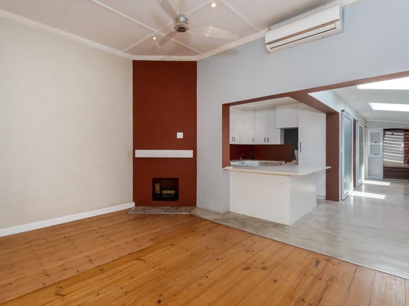 Open-plan living area featuring timber flooring, a fireplace, and a connected kitchen with white cabinetry and a breakfast bar.