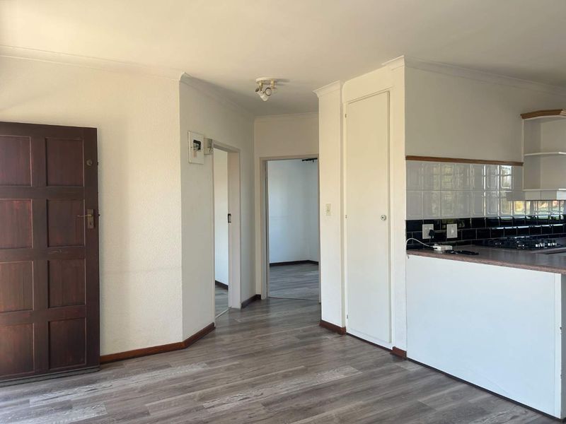 Open plan living area featuring laminate flooring, a built-in storage cupboard, and a kitchen section with tiled backsplash, leading to adjacent rooms.