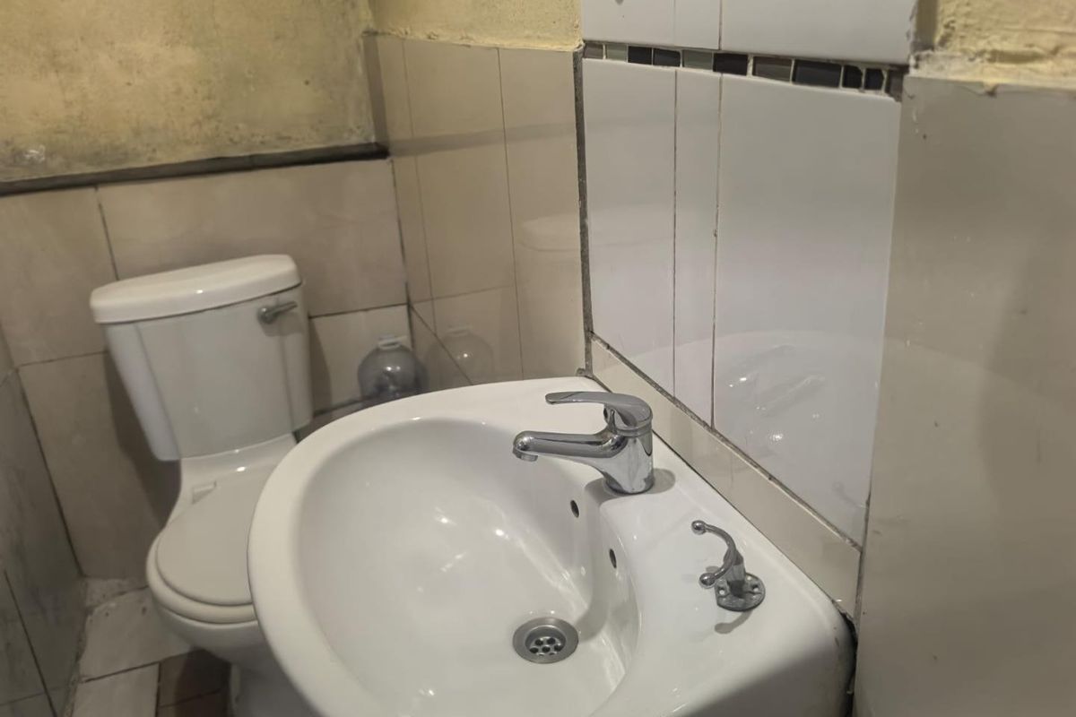 A compact bathroom featuring a wall-mounted basin and standard toilet, requiring cosmetic updates to the wall finishes and tiling.
