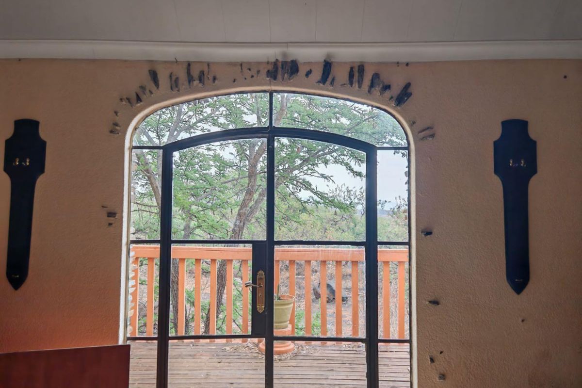 Interior view featuring an arched metal-framed glass door leading to an outdoor wooden deck, showing signs of wear on the surrounding wall.