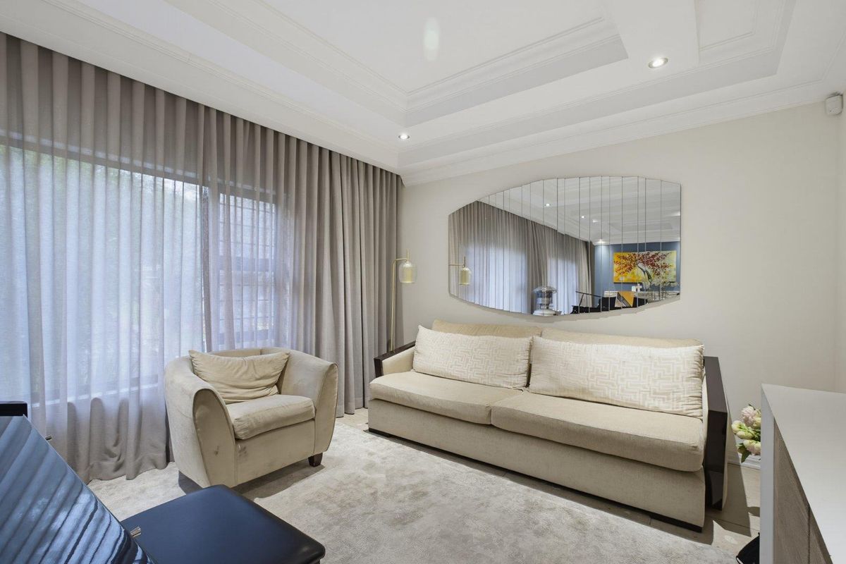 A well-appointed living room featuring recessed tray ceiling lighting, large windows with floor-to-ceiling curtains, and a neutral color palette.