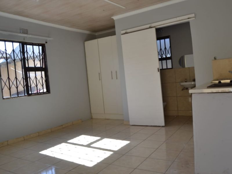 Open plan living area featuring tiled floors, built-in cupboards, and a compact kitchenette, with direct access to an adjoining bathroom.