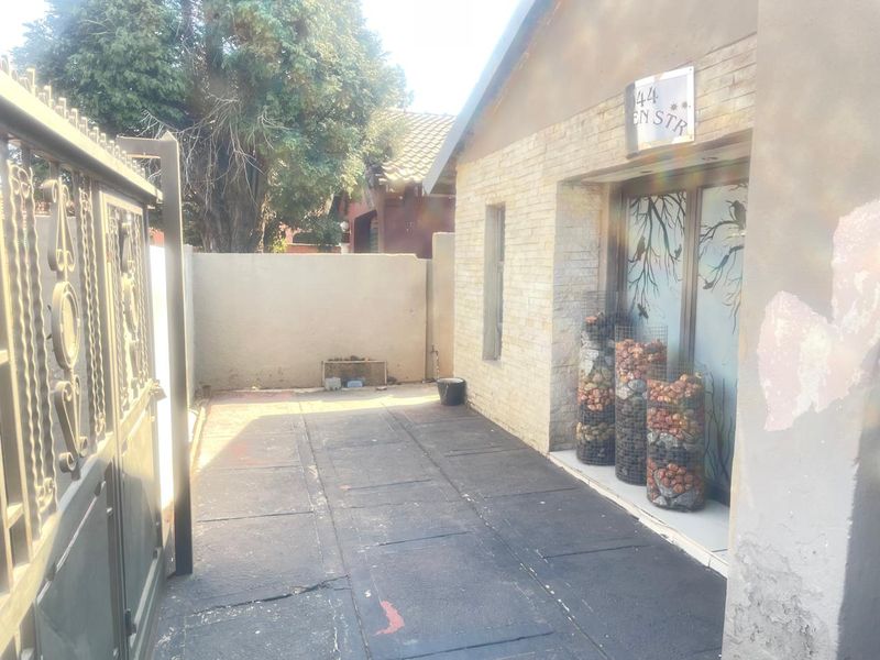 Front entrance area featuring a metal security gate, paved driveway, and brick facade with visible wear on the exterior walls.