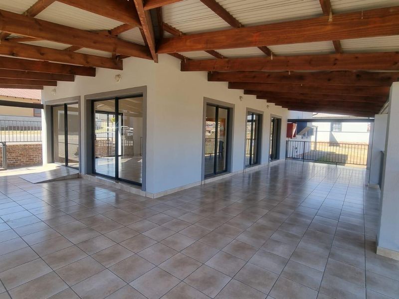 Spacious covered patio featuring exposed timber beams, tiled flooring, and multiple sliding glass door access points, ideal for outdoor entertaining.
