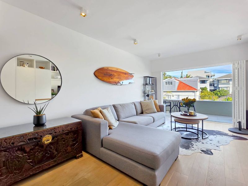 A bright and modern living room featuring engineered timber flooring, recessed ceiling lighting, and seamless access to an outdoor balcony.
