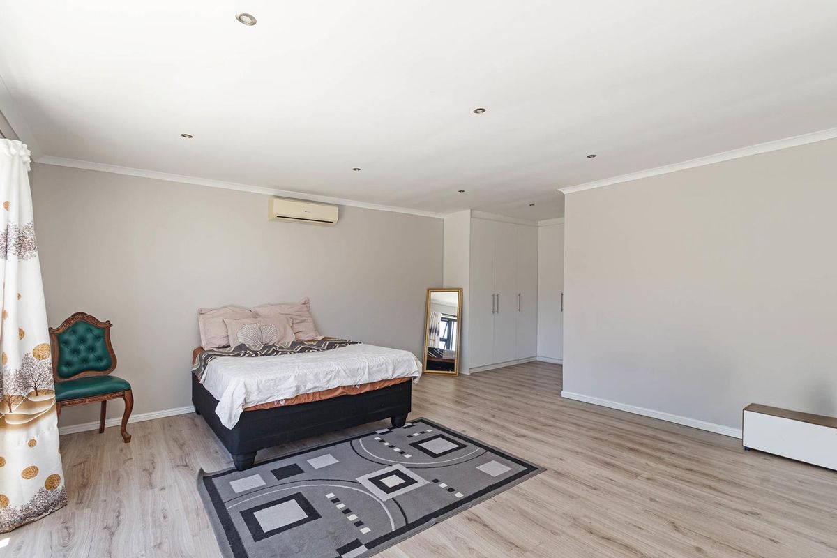 Spacious bedroom featuring light laminate flooring, built-in cupboards, recessed downlights, and a wall-mounted air conditioning unit.