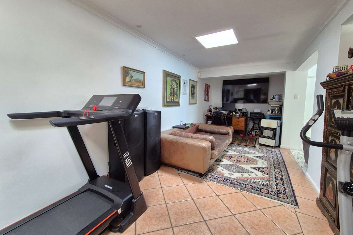 A multi-purpose living area featuring tiled flooring and a skylight, currently utilized as a combined lounge and home office space.