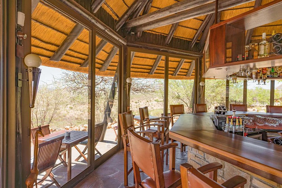 A rustic bar area featuring a thatched roof, stone-clad bar counter, and large glass sliding doors opening to a scenic landscape view.