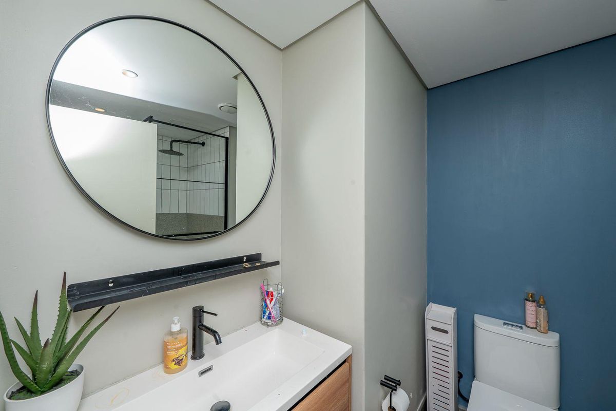 Modern bathroom featuring a vanity with a black faucet, a round mirror, and a separate shower area with tiled walls and black fixtures.