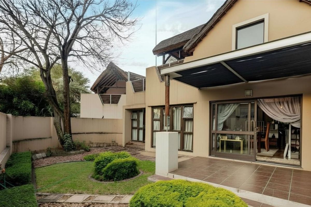 Rear view of the apartment featuring a tiled patio, sliding glass doors, and a private garden area with established landscaping and a thatched roof.