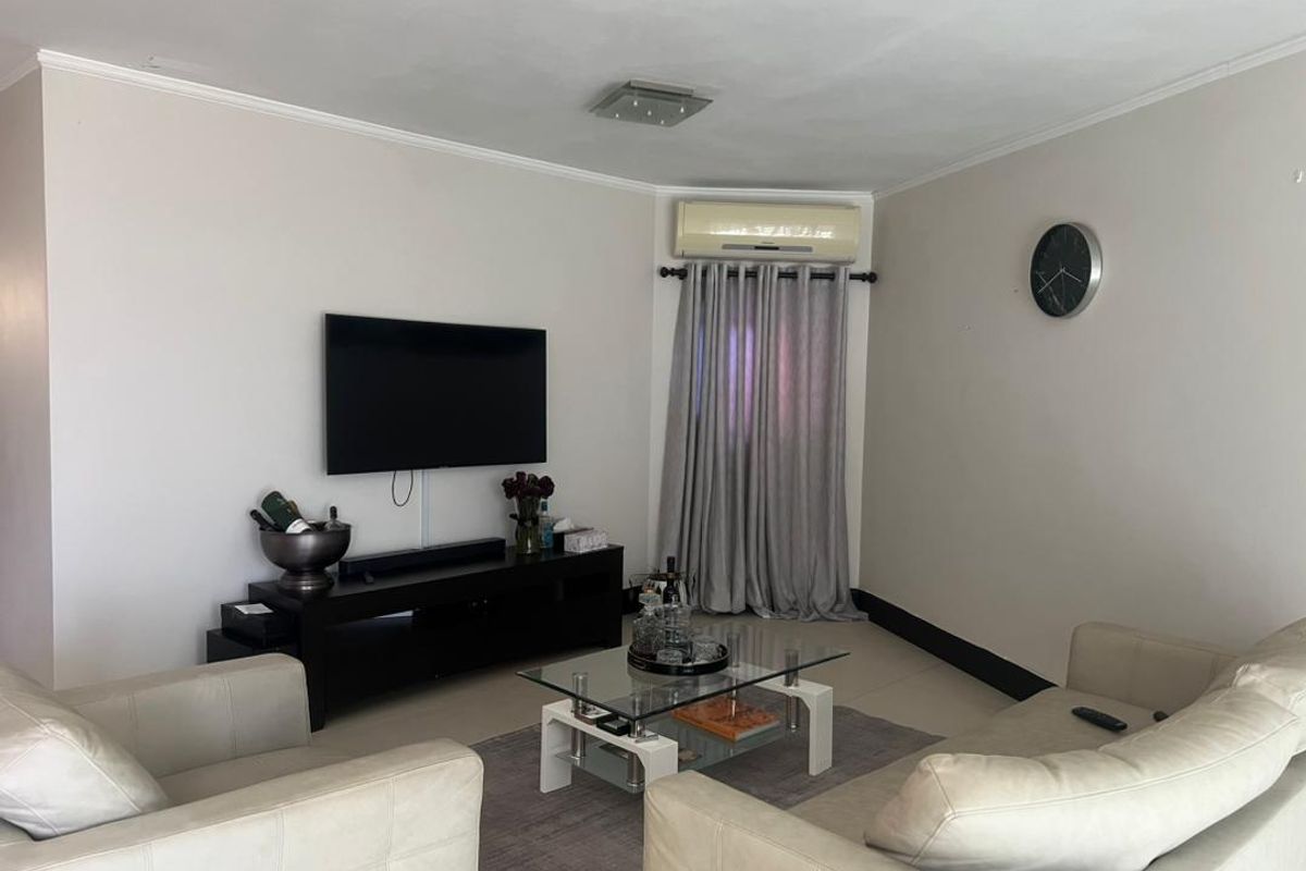 A comfortable living room featuring tiled flooring, a wall-mounted air conditioning unit, and neutral wall finishes.