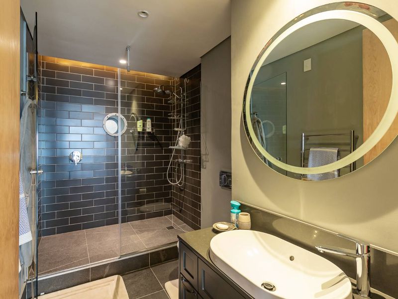 Modern bathroom featuring a walk-in shower with dark subway tiles, a sleek vanity with a vessel sink, and a backlit circular mirror.
