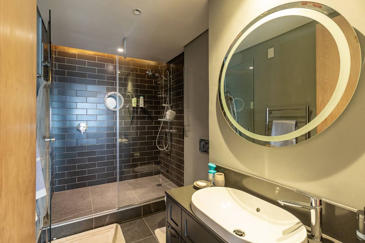 Modern bathroom featuring a walk-in shower with dark subway tiles, a sleek vanity with a vessel sink, and a backlit circular mirror.