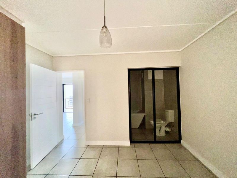 An empty bedroom featuring tiled flooring, a pendant light, and a sliding glass door leading to an en-suite bathroom.