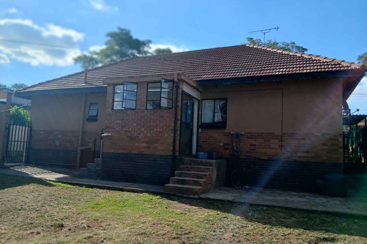 Rear view of the house featuring a brick facade, tiled roof, and a small concrete patio area leading to the backyard.