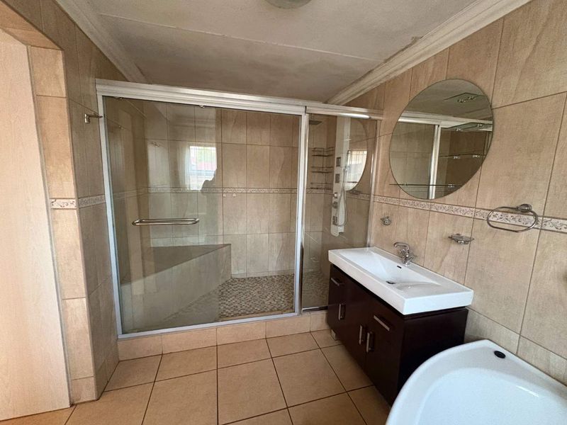 A functional bathroom featuring a walk-in shower with glass enclosure, a vanity basin, and neutral wall and floor tiling.
