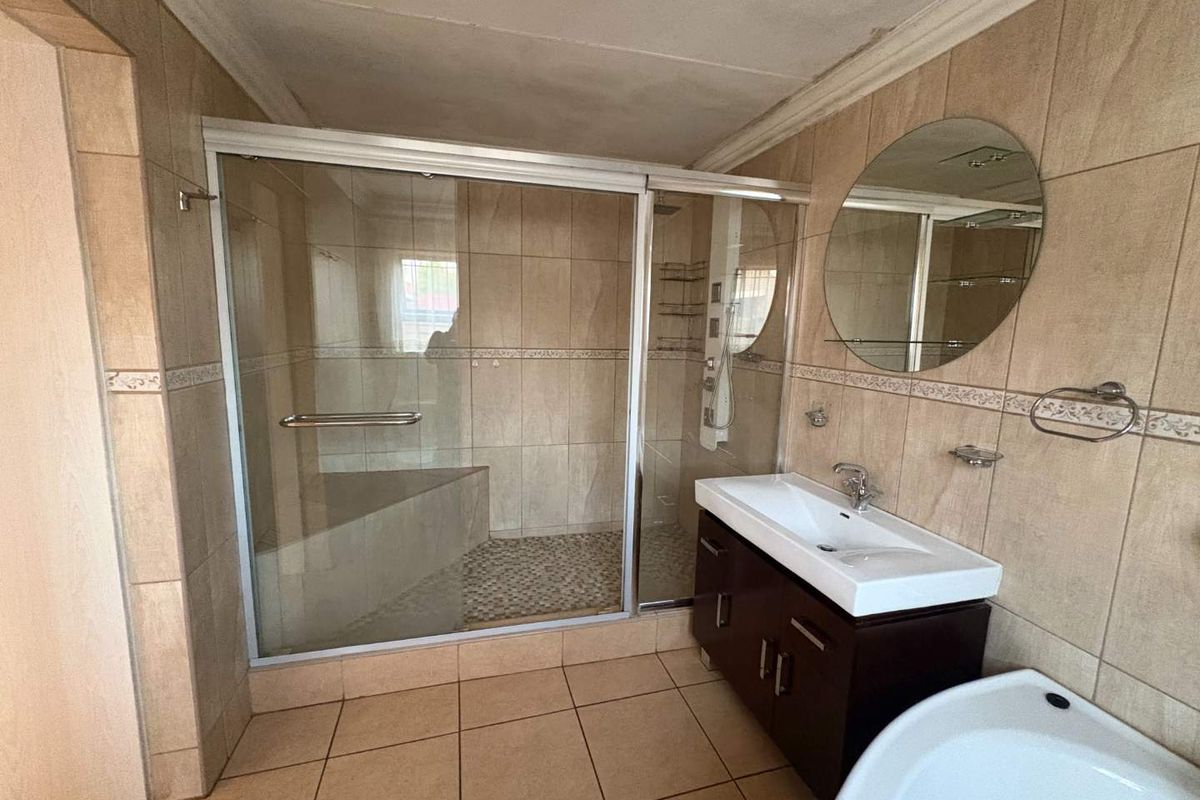 A functional bathroom featuring a walk-in shower with glass enclosure, a vanity basin, and neutral wall and floor tiling.