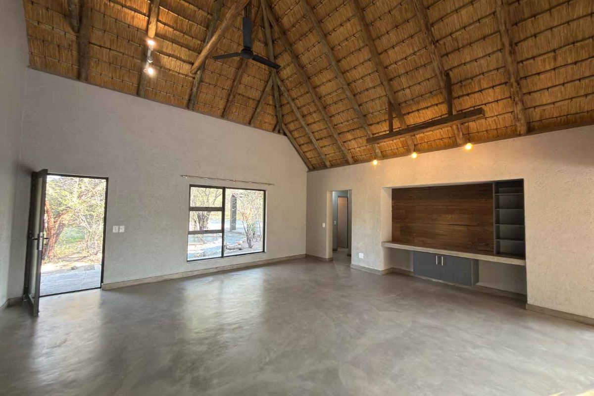 Spacious living area featuring a high vaulted thatched ceiling, polished concrete flooring, and a built-in media unit with timber paneling.